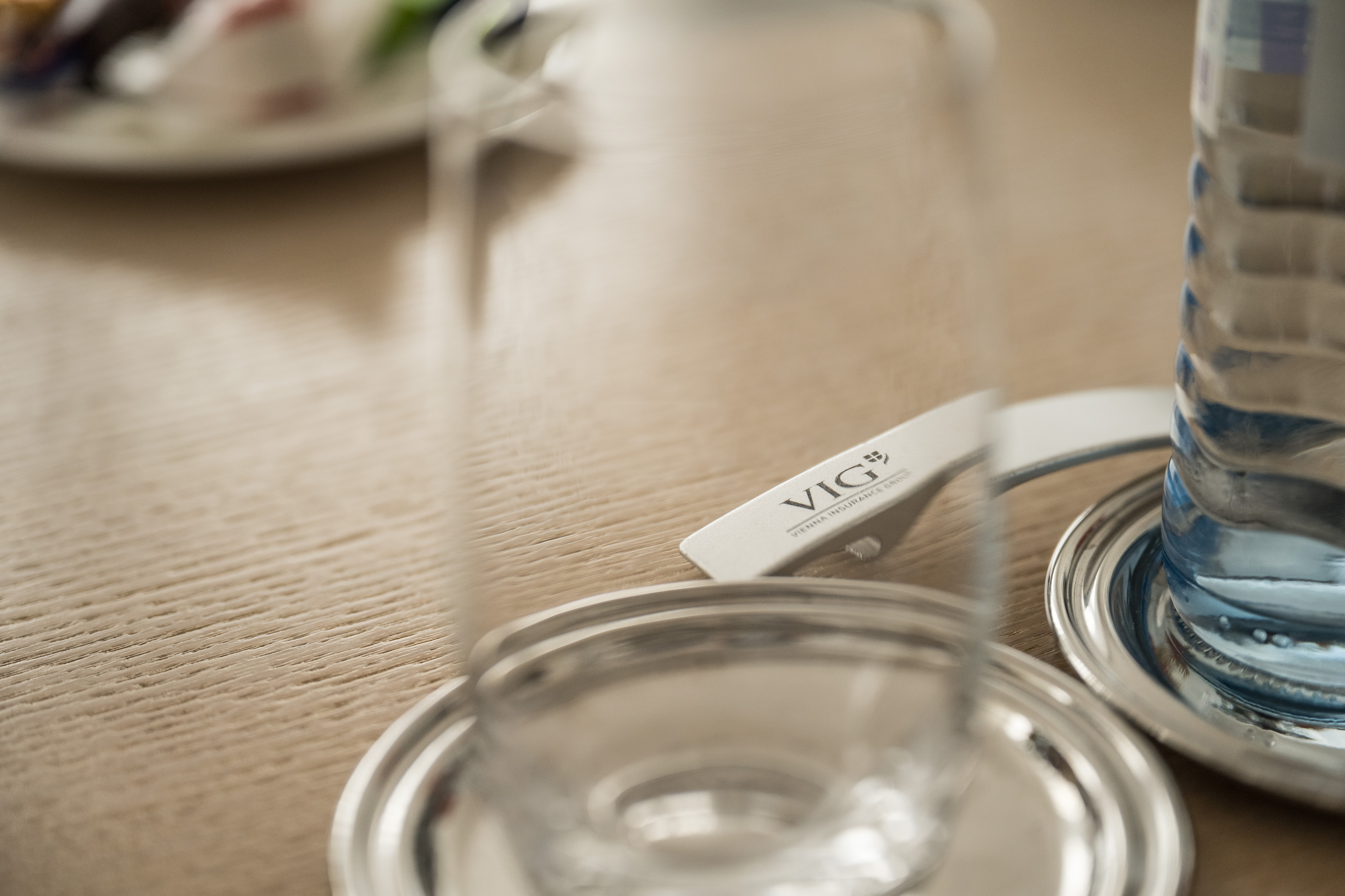 Meetringraum-Stilleben: Trinkglas, Wasserflasche und Flaschenöffner mit VIG-Logo.
