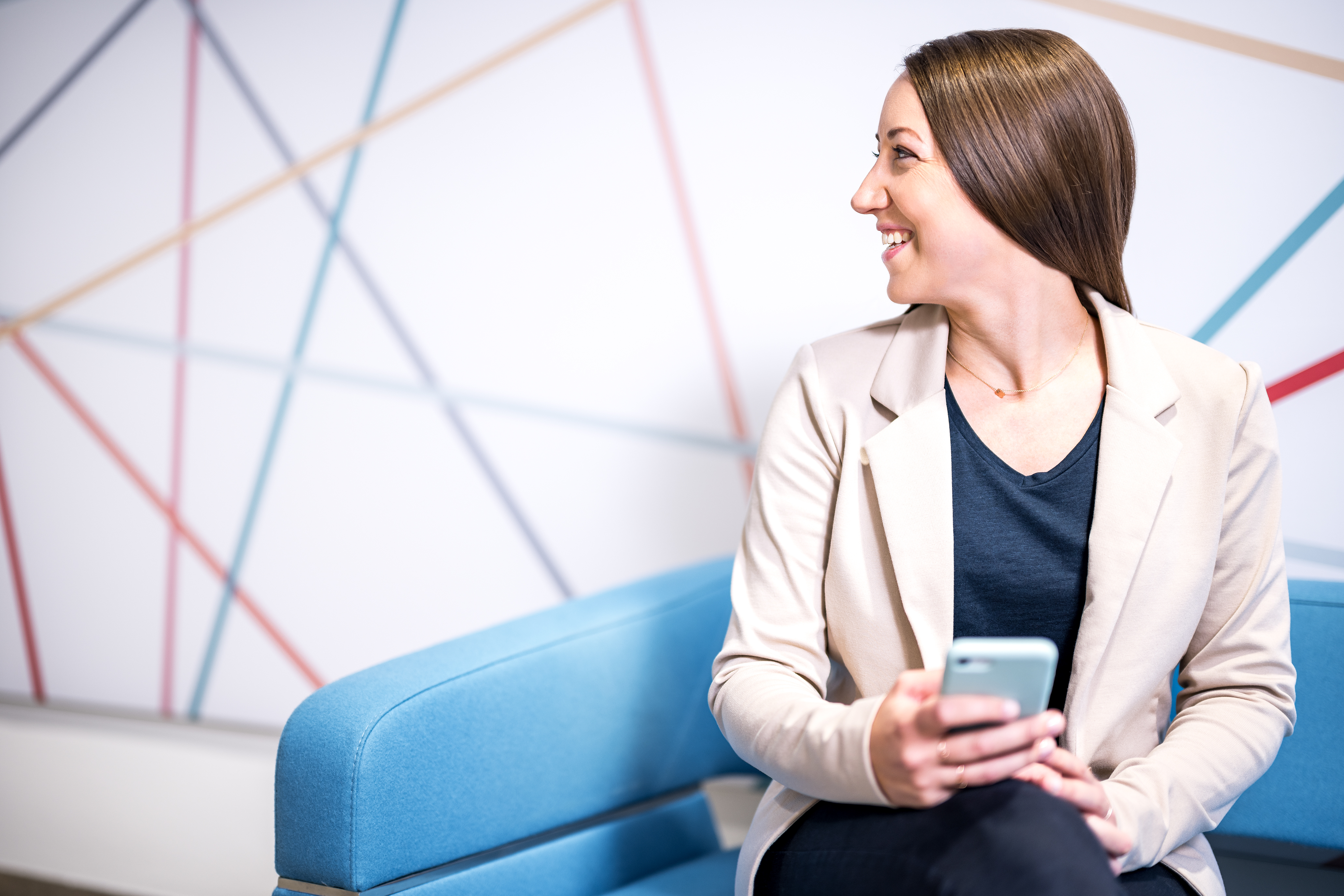VIG employee is sitting on a blue Sofa with mobile phone in her hands