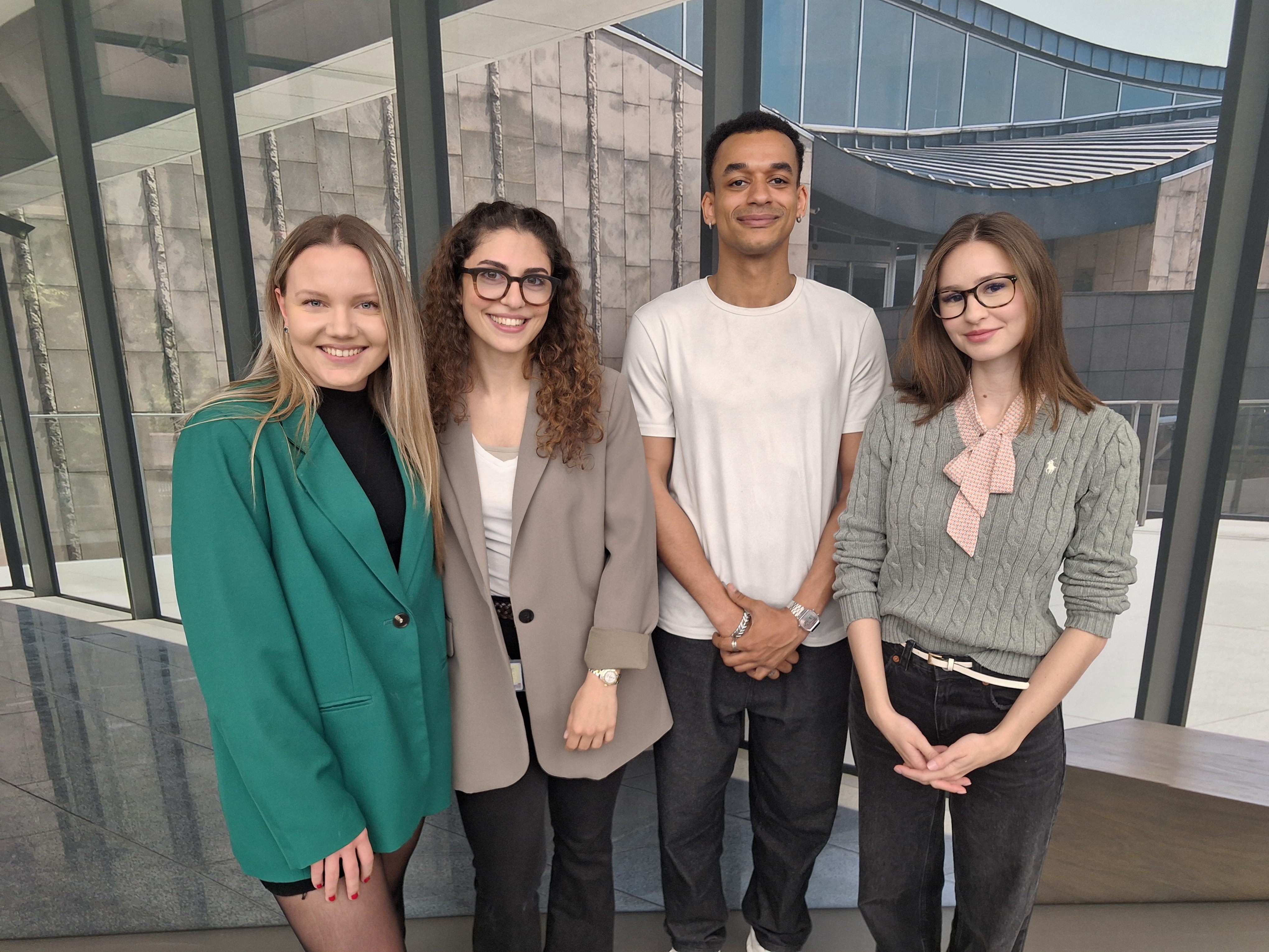 Drei junge Frauen und ein junger Mann lächeln freundlich. 