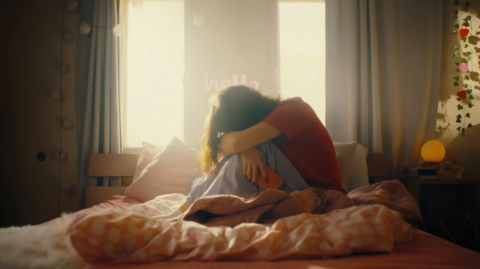 Person sitzt im Bett mit angezogenen Knien und hat den Kopf auf die Knie abgelegt.