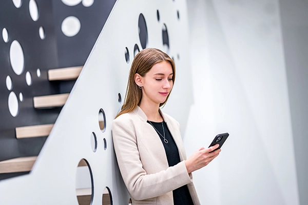 Young VIG employee leans against futuristic staircase and checks her mobile phone
