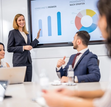 © Michael Kammeter In einem Meetingraum präsentiert eine Frau Zahlen auf einer Leinwand einer Gruppe von drei Personen