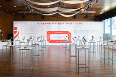VIG HV 2026: Speisesaal; Stehtische vor Plakatwand