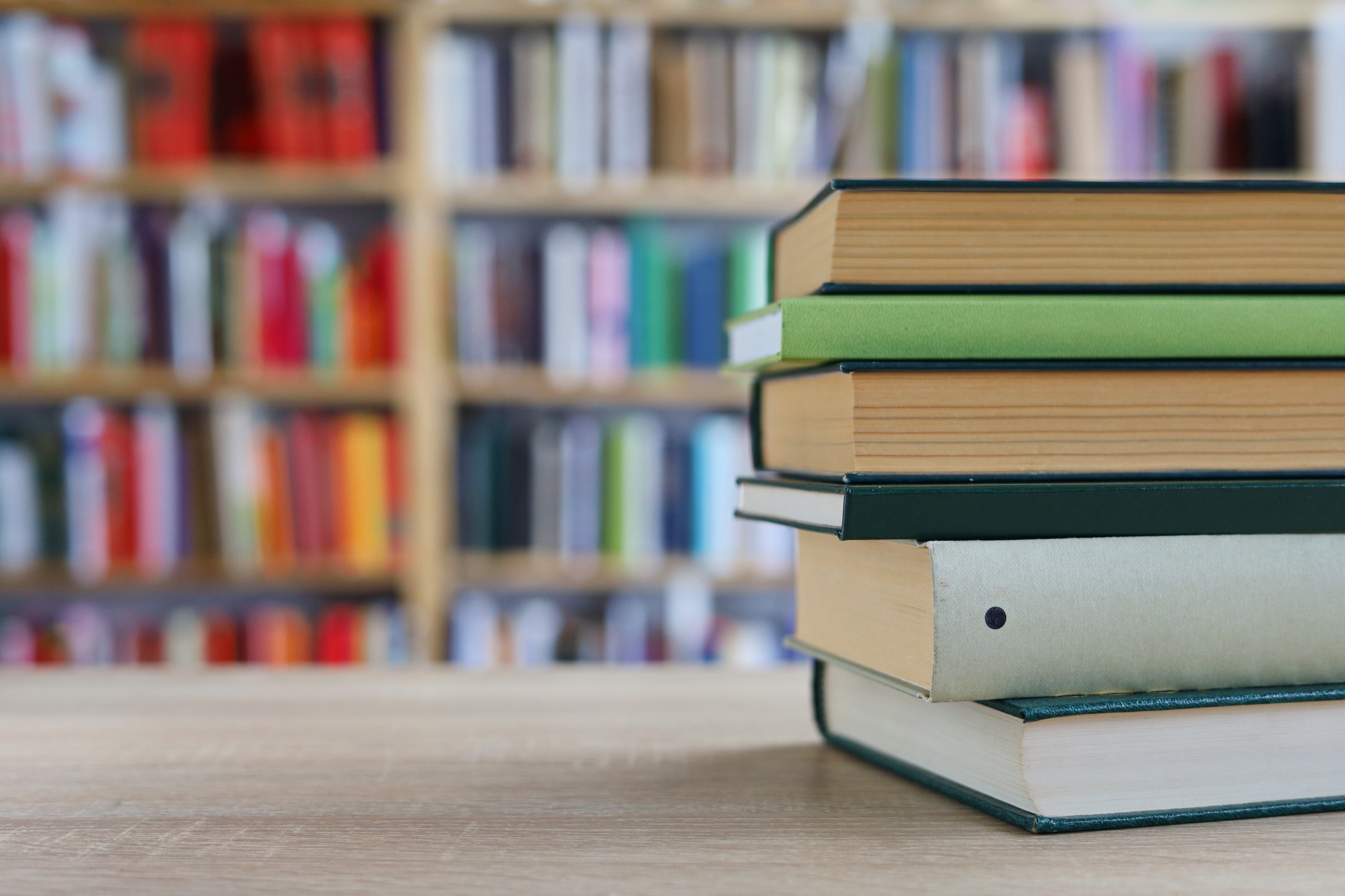 Stacked books on a table with full bookshelves in the background.