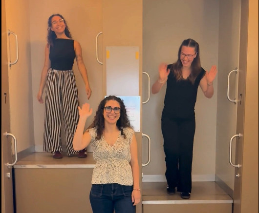 3 female student workers inside and in front of the Paternoster, waving to one another