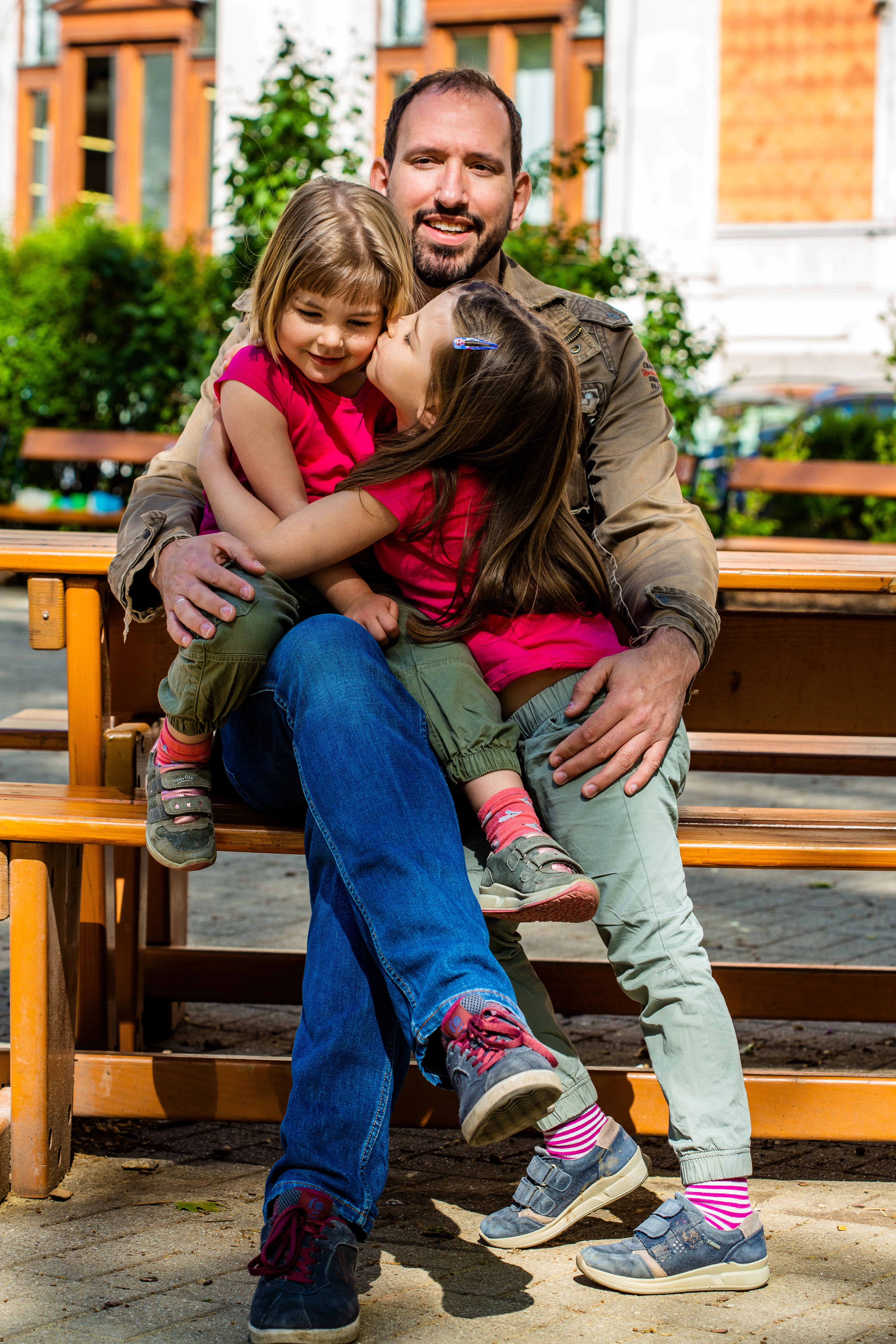 Dad hugs his two children sitting on a park bench