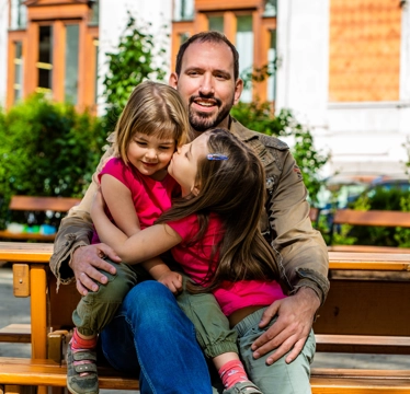 © Martin Marschall Papa umarmt seine beiden Kinder sitzend auf einer Parkbank