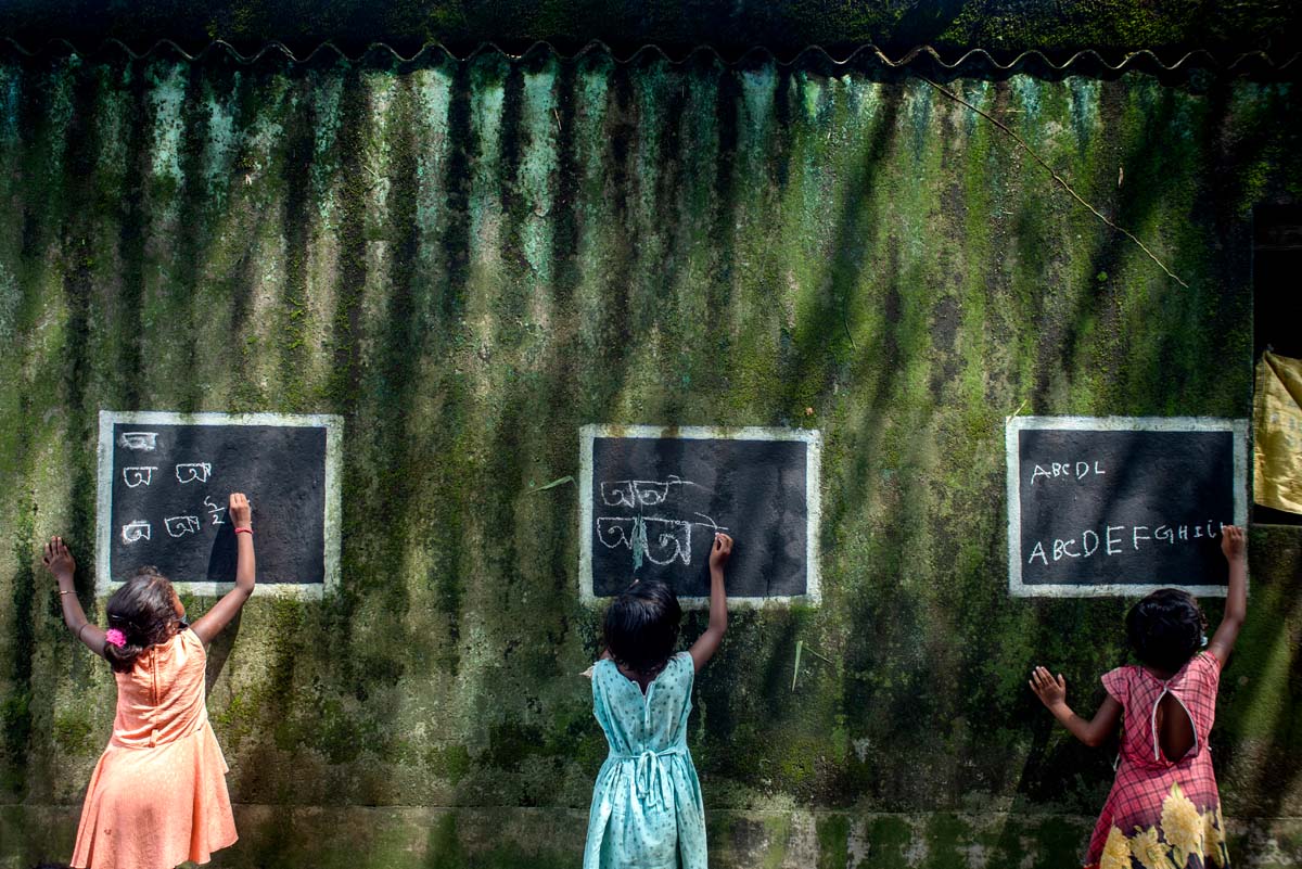 Gewinnerbild des Global Peace Photo Awards 2022 von Sourav Das namens Blackboard Work. Drei kleine Mädchen schreiben mit Kreide auf drei Tafeln.