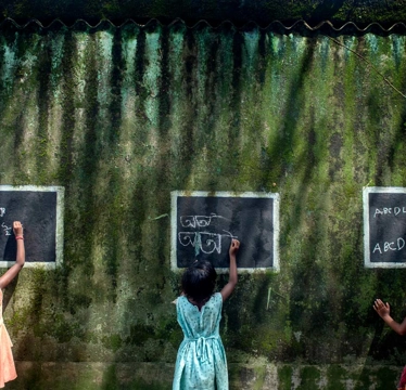 © Sourav Das Gewinnerbild des Global Peace Photo Awards 2022 von Sourav Das namens Blackboard Work. Drei kleine Mädchen schreiben mit Kreide auf drei Tafeln.